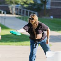 Woman playing Kan-Jam game on Kirkhof Lawn with woman walking behind.